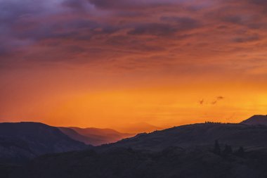 Atmosferik manzara. Dağların siluetleriyle. Arkasında ağaçlar olan. Günbatımının ya da aydınlatıcı rengin gün doğumunun olduğu renkli doğa manzarası. Günbatımı ödemesi