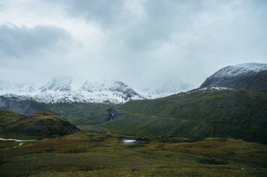 Düşük bulutlu, bulutlu, karlı dağlarla kaplı minimalist dağlık bir arazi. Düşük bulutlu gökyüzünün altında karlı dağ sıraları olan güzel bir manzara. Yüksek dağlarda atmosfer minimalizmi.