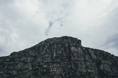 Bulutlu gökyüzünün altında kayalık dağ silueti olan karanlık atmosferik asgari manzara. Bulutlu havada dağ silueti olan minimalist dağ manzarası. Bulutların altında kara kayalar olan minimalizm