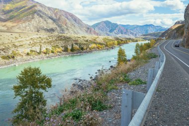 Sonbaharda gün ışığında dağ yolunda büyük dağ nehri boyunca giden araba. Geniş turkuaz nehir ve dağ yolu. Sonbaharda dağlarda otoyol. Rusya, Altai Cumhuriyeti, Chuysky yolu, 19 Eylül 2020.