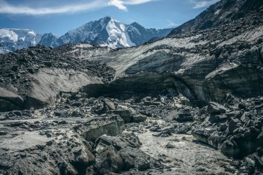 Büyük karlı dağların arka planında, buzuldan başlayan güçlü dağ nehrinin bulunduğu manzara. Çalkantılı dağ nehrinin kaynağında buzullu güzel bir manzara..