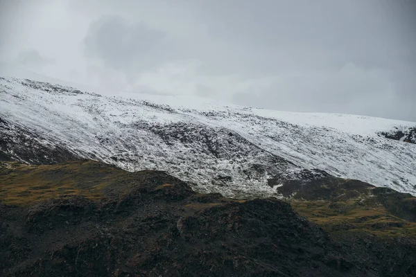 雪と最小限の高地の風景 曇りの空の下で山のキャップ 曇りの天気で雪に覆われた高い山の範囲 緑の山々 白い雪と灰色の空と大気ミニマリズム — ストック写真
