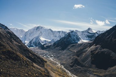 Büyük karlı dağları ve dağlık nehri olan güzel bir dağ manzarası. Sonbahar renklerinde kayaların arasında vadide birçok dere var. Gün ışığında. Sonbaharda yüksek kar duvarı olan güneşli bir manzara.