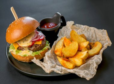 Siyah arka planda siyah tabakta hamburger ve patates kızartması.