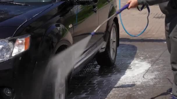 Vaske en bil med vandtryk på en selvbetjeningsstation. Mand vasker sin beskidte bil efter en lang rejse – Stock-video
