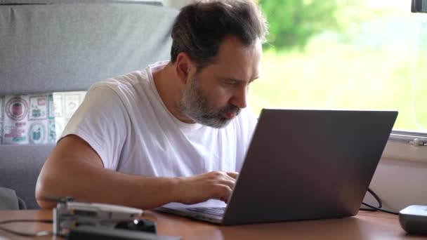 Men with Modern Laptop Computer in His Hands Working Remotely While Camping in RV Camper Van Motorhome. Work and Travel Theme. — Vídeo de Stock