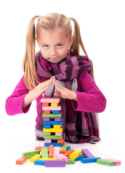 Pasatiempos para niños, creatividad, una niña con un vestido azul jugando con el juego de madera jenga sobre fondo blanco —  Fotos de Stock