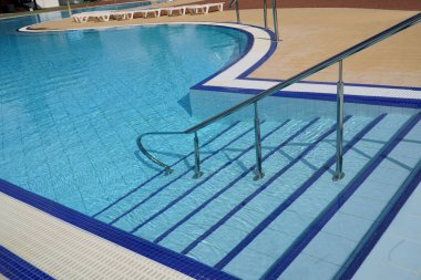 Demiryolu ve merdivenler açık havuzun mavi sularından aşağı iniyor.