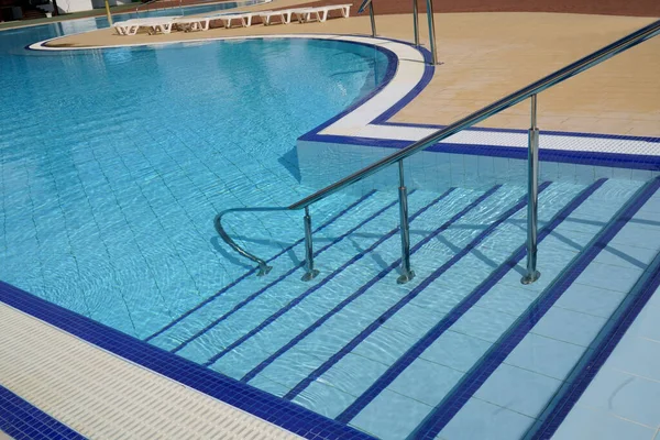 Railings and stairs going down the blue water of an outdoor swimming pool