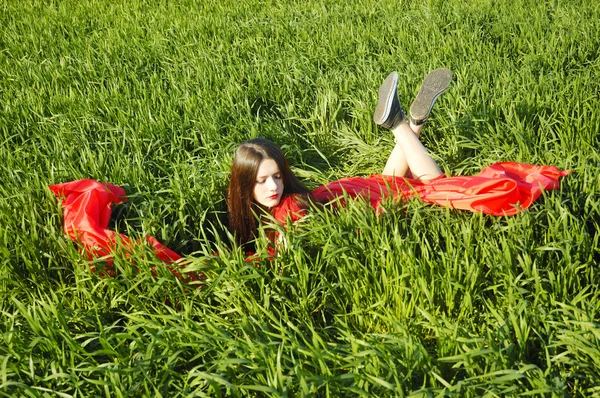 Young lady in red dress lie on field — Stock Photo, Image