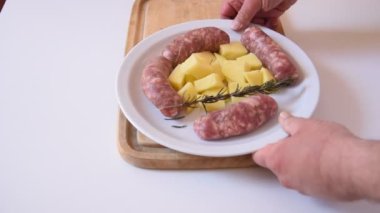 Beyaz tabakta patates garnitürlü rezeneli sosisler.