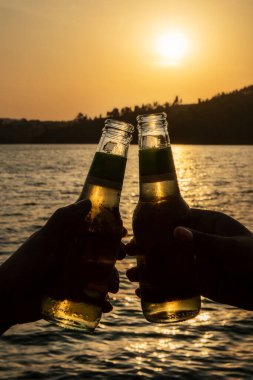 Dostlar gün batımında nehrin kenarında kadeh kaldırıyor. Altın içki..