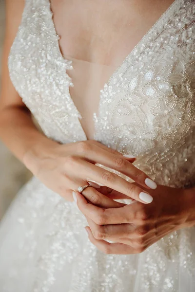 Hands of the bride in a white wedding dress with a gold engagement ring with a diamond close-up. Bride touches the ring with her fingers