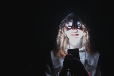 Açık renk kazaklı genç bir kız karanlıkta poz veriyor.