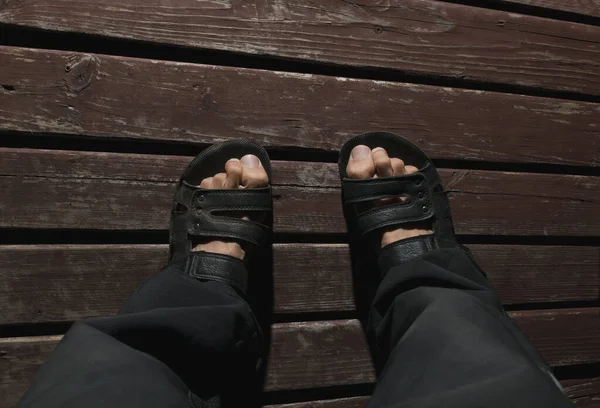 The feet of an adult man in slippers on a wooden platform in the dark