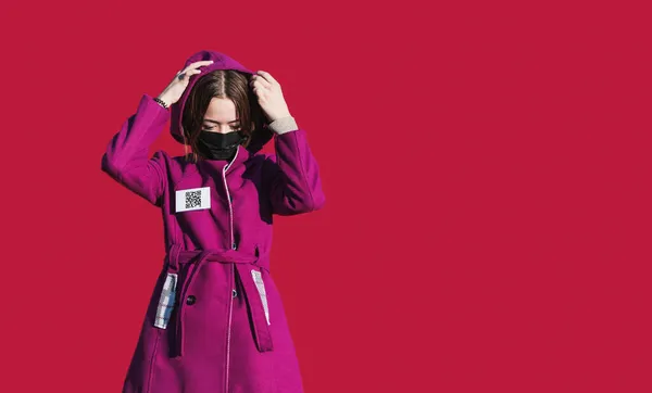 赤い背景にバッジとQrコードを持つ暖かいコートの若い女の子 — ストック写真