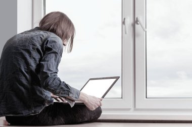 Pencerenin yanında dizüstü bilgisayarı olan genç bir adam oturuyor.