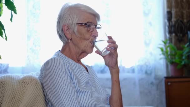 ポートレート｜caucasian健康的なシニア大人の女性が自宅で新鮮なミネラル純水を飲んでガラスを保持します。健康を維持するということです. — ストック動画