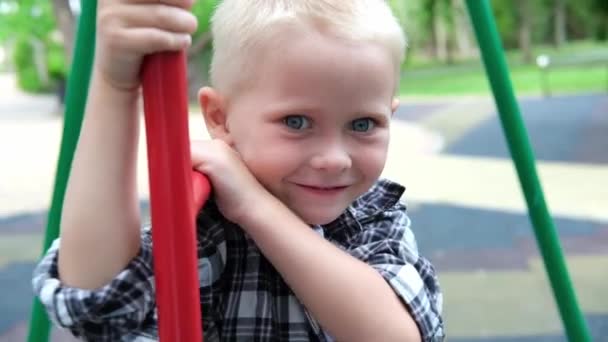 Портрет милий світле волосся хлопчик з блакитними очима грає на ігровому майданчику. діти дитина посміхається і дивиться на камеру в парку на заході сонця. щаслива концепція сімейної мрії. повільний рух — стокове відео