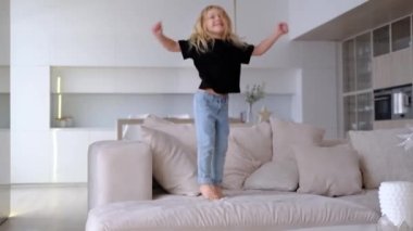 Siyah tişört ve kot pantolon giyen, oturma odasındaki yastıklarla kanepede zıplayarak gülen sevimli, kıvırcık saçlı kız portresi. Yalnız mutlu sevimli çocuk yatakta eğleniyor.. 