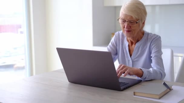 Ältere ältere Frau arbeitet am Laptop in der Küche zu Hause im Büro. Frau sieht Business-Training, Online-Webinar am Computer. Fernarbeitendes soziales Fernlernen von zu Hause. 60er-Jahre-Frau — Stockvideo
