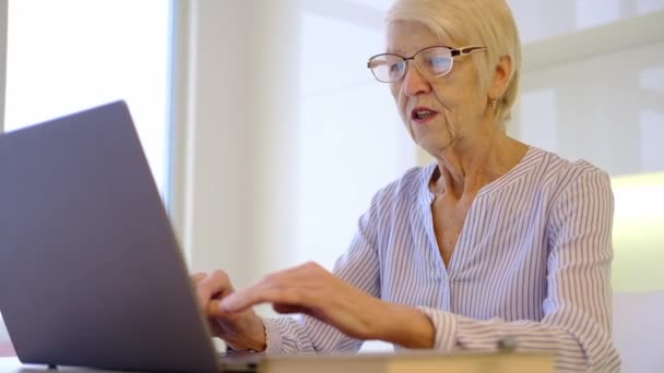 Starsza, dojrzała kobieta pracująca na laptopie w domu w biurze. Pani ogląda szkolenia biznesowe, webinarium online na komputerze. zdalne uczenie się na odległość w pracy z domu. Kobieta lat 60. — Wideo stockowe