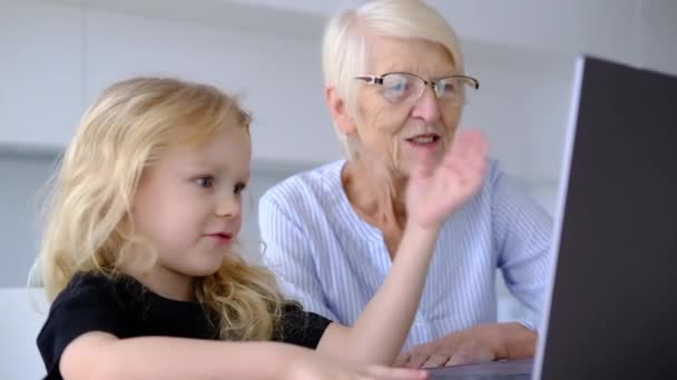 Elderly caucasian woman grandmother and little curly granddaughter using laptop in the kitchen at home. online learning concept. woman with child spend time together — Vídeo de Stock