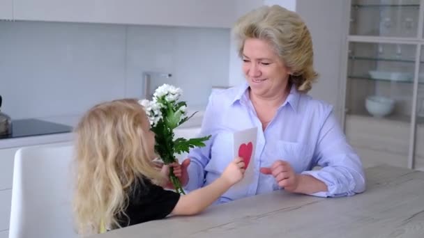 Szczęśliwy cute kręcone małe dziecko wnuczka obejmująca całowanie starą babcię. dziewczyna prezentuje kwiat bukiet dla starszej pani co niespodzianka na urodziny, przytulanie zabawy — Wideo stockowe
