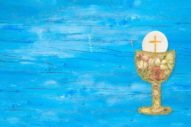 First holy communion invitation card. Flowers and gold  chalice  on a  blue wooden background with copy space to text and photo.