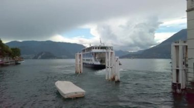 Varenna, Como Gölü, Lombardy, İtalya 'daki rıhtımdan kalkan bir feribotun kısa bir klibi. Bulutlu, bulutlu bir yaz günü, sadece birkaç mavi gökyüzü lekesi var. Arka planda gölü çevreleyen dağlar var. 4K
