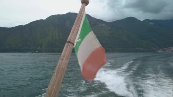 コモ湖のボートで風になびくイタリアの国旗 背景には山があります 船はレノに向かって航行している 曇り空の夏の日 — ストック動画
