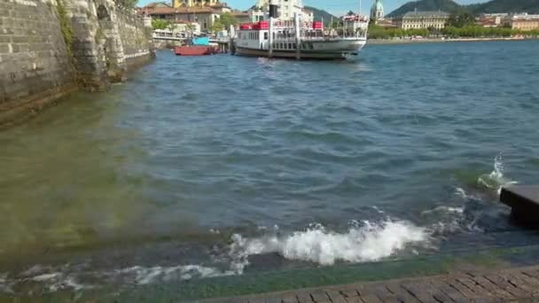 意大利伦巴第科莫市科莫湖的一个混凝土码头被小海浪击中 在背景上有一个旅游渡船 还有一个美丽的科莫市的美景 这是一个阳光明媚的夏日 4K夹 — 图库视频影像