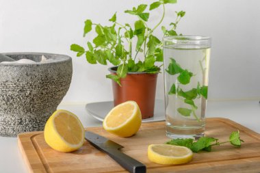 Kavanozda nane şekeri, bardakta dilimlenmiş limon ve doğrama tahtasındaki siyah bıçak. Bardakta sıcak su var. Arınmak ve sağlıklı bir yaşam tarzı. Arka planda granit havan topu var.