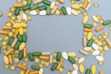 Various medicine pills scattered on a grey background. There is copy space in the middle. Many different colors, shapes and sizes. Perfect for both topics of abuse and of health