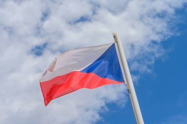 Czech Republic flag waving in the wind. It is a beautiful sunny summer day, with blue sky and white clouds in the background.