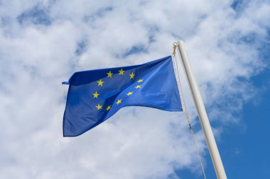 European Union flag waving in the wind. It is a beautiful sunny summer day, with blue sky and white clouds in the background.