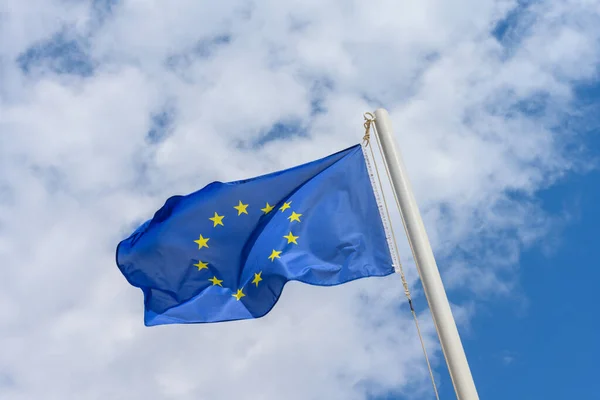 European Union flag waving in the wind. It is a beautiful sunny summer day, with blue sky and white clouds in the background.