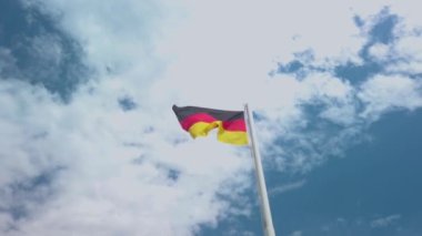 Rüzgarda sallanan Alman bayrağı. Çok güzel güneşli bir yaz günü, mavi gökyüzü ve beyaz bulutlar arka planda. 4K stok video