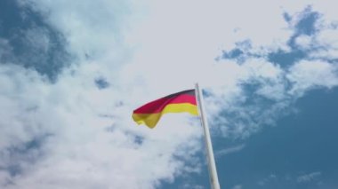 Rüzgarda sallanan Alman bayrağı. Çok güzel güneşli bir yaz günü, mavi gökyüzü ve beyaz bulutlar arka planda. 4K stok video yavaş çekim