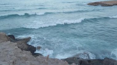 Dalgalar İspanya 'da La Zenia sahilindeki kayalara çarpıyor. Suyun güzel bir açık mavi rengi var. Çok güzel bir yaz akşamı. Güçlü akımı sembolize eden video mu yoksa sadece tatil için mi? Yavaş çekim