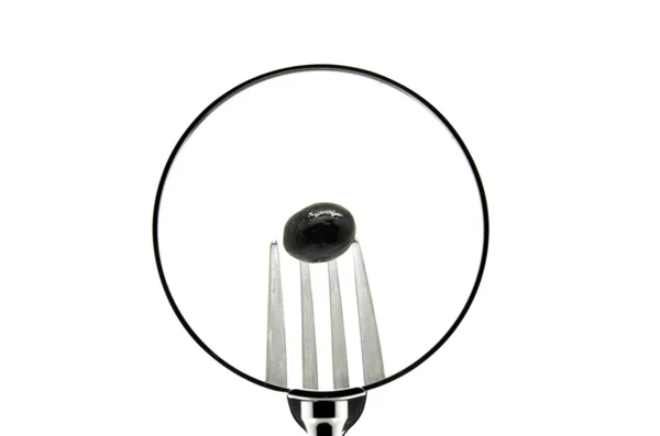 An olive in a fork punctured seen behind a magnifying glass — Stock Photo, Image