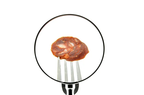 O bucată de cârnați pe o furculiță perforată văzută în spatele unei lupe — Fotografie, imagine de stoc