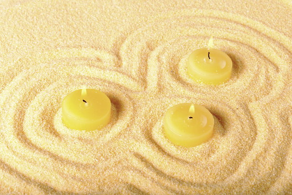 Three lighted yellow candles on the sand