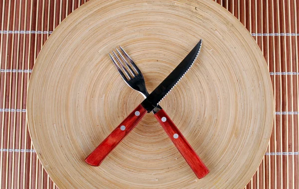 Wooden round dish and red cutlery on bamboo — Stock Photo, Image