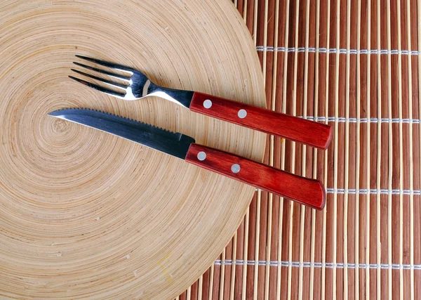 Wooden round dish and red cutlery on bamboo — Stock Photo, Image