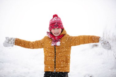 Kar yağarken dışarıda oynayan renkli elbiseli komik küçük çocuk. Soğuk karlı günlerde çocuklarla aktif tatiller. Mutlu çocuk kışın eğleniyor ve oynuyor..