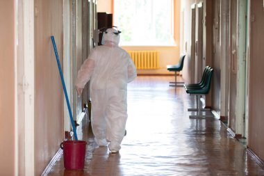 Belarus, Gomil şehri 31 Mayıs 2021 Bölge Hastanesi. Koronavirüs enfeksiyonu sırasında koruyucu kıyafetli bir temizlikçi kadın hastane koridorunda duruyor..