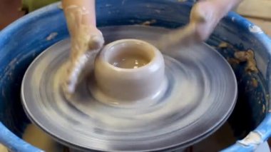 Bir çömlekçinin ellerine yakın çekim ve çömlekçinin tekerine takılmış bir çocuk eli. Çamurla çalışmak. Clay atölyesi. Sanatsal eğitim.