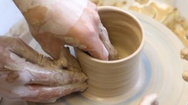 Bir çömlekçinin ellerine yakın çekim ve çömlekçinin tekerine takılmış bir çocuk eli. Çamurla çalışmak. Clay atölyesi. Sanatsal eğitim.
