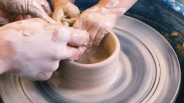 Bir çömlekçinin ellerine yakın çekim ve çömlekçinin tekerine takılmış bir çocuk eli. Çamurla çalışmak. Clay atölyesi. Sanatsal eğitim.